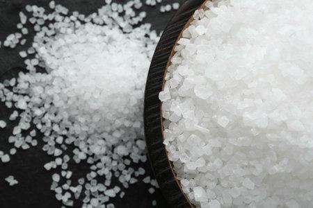 Plate with natural sea salt on black table, closeup. Space for text