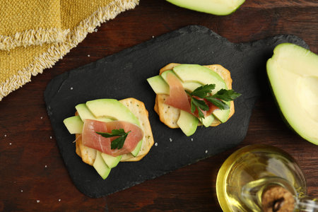 Delicious crackers with avocado, prosciutto and parsley on wooden table, flat layの写真素材