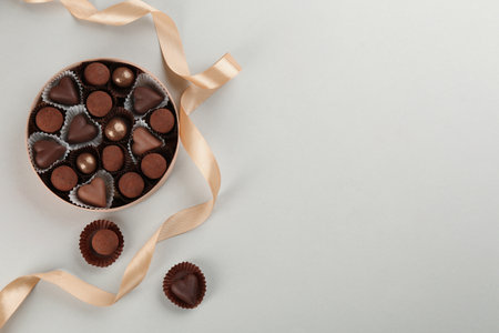 Different delicious chocolate candies in box and ribbon on light background, flat lay. Space for textの写真素材