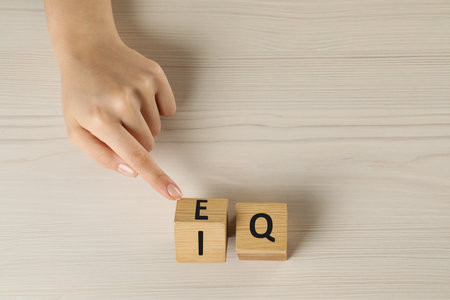 Woman turning cube with letters E and I near Q at white wooden table, above view. Space for textの写真素材
