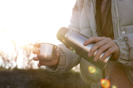 Woman pouring hot drink into cup from thermo outdoors, closeupの写真素材