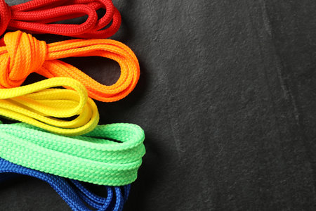 Colorful shoelaces on black background, flat lay. Space for text