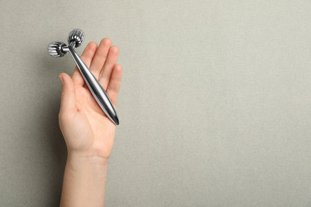 Woman with metal face roller on gray background, top view. Space for textの写真素材