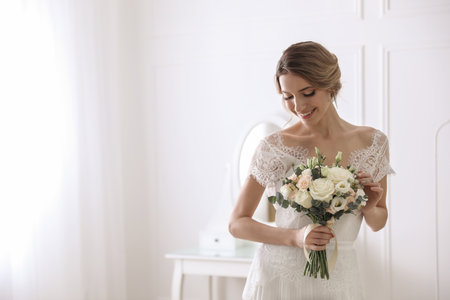 Bride in beautiful wedding dress with bouquet indoors. Space for textの写真素材