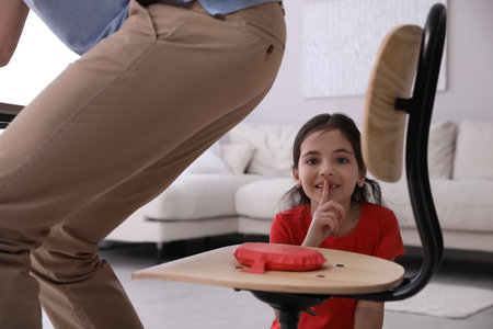 Cute little girl putting whoopee cushion on father's chair while he sitting down at home, closeupの写真素材