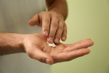 Man applying cream onto hand on green background, closeupの写真素材