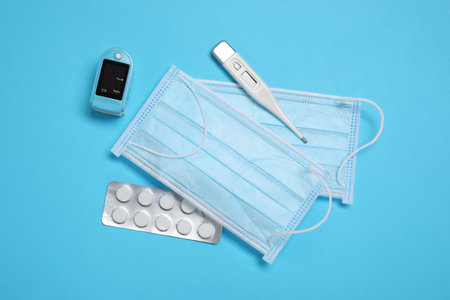 Flat lay composition with thermometer, pills and medical masks on light blue backgroundの写真素材