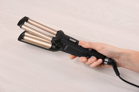 Woman holding modern triple curling iron on wooden background, closeupの写真素材