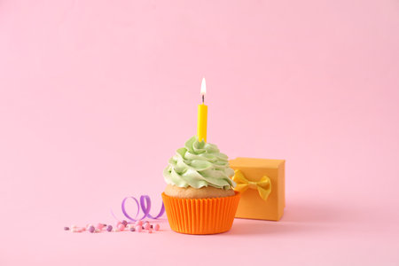 Birthday cupcake with burning candle and gift box on pink backgroundの写真素材