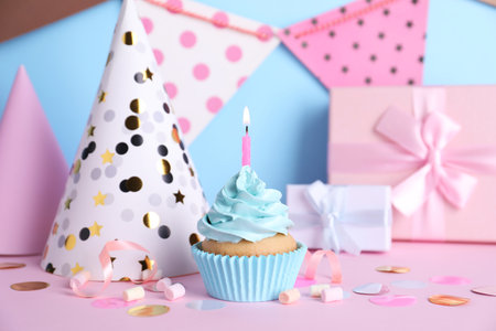 Delicious birthday cupcake with burning candle, marshmallows and party decor on color backgroundの写真素材