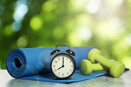 Alarm clock, yoga mat and dumbbells on marble table outdoors. morning exerciseの写真素材