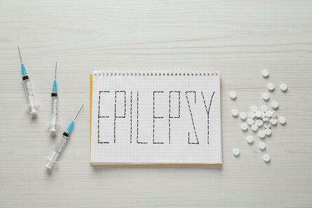 Notebook with word Epilepsy, pills and syringes on white wooden table, flat layの写真素材