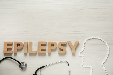 Human head silhouette made of pills, word Epilepsy and stethoscope on white wooden table, flat lay. Space for textの写真素材