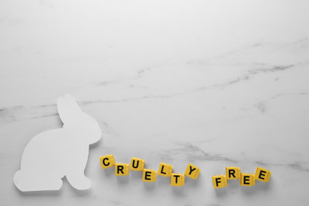Flat lay of cubes with phrase Cruelty Free and rabbit figure on white marble table, space for text....