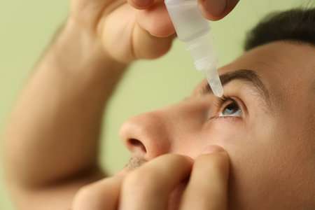 Man using eye drops on green background, closeupの写真素材