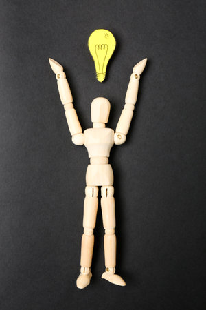 Wooden puppet and paper lightbulb on black background, flat layの写真素材