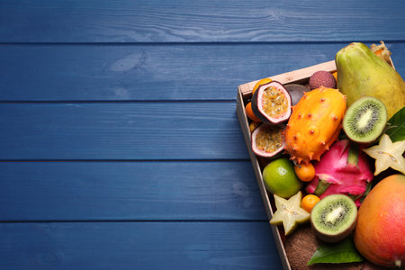Crate with different exotic fruits on blue wooden table, top view. Space for textの写真素材
