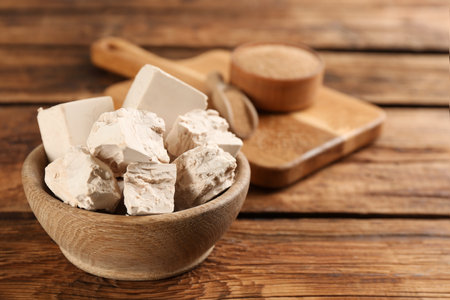 Bowl with pieces of compressed yeast on wooden table, closeup. Space for textの写真素材