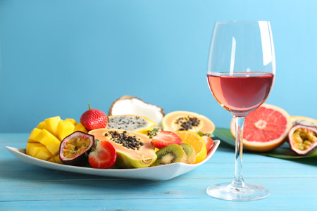 Delicious exotic fruits and glass of wine on light blue wooden tableの写真素材