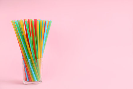 Colorful plastic drinking straws in glass on pink background, space for text