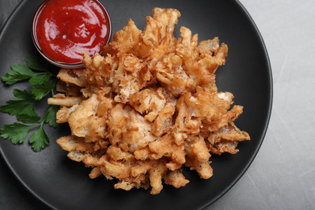 Delicious onion blossom with ketchup served on black table, top view