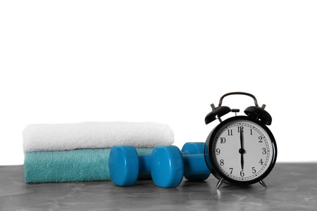 Alarm clock, towels and dumbbells on marble table against gray background. morning exerciseの写真素材