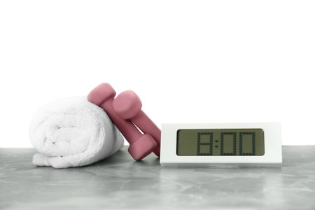 Digital clock, towel and dumbbells on marble table against gray background. morning exerciseの写真素材