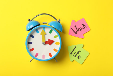 Alarm clock and sticky notes on yellow background, flat lay. Life work balance conceptの写真素材