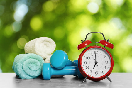 Alarm clock, towels and dumbbells on marble table outdoors. morning exerciseの写真素材