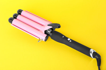 Modern triple curling iron on yellow backgroundの写真素材