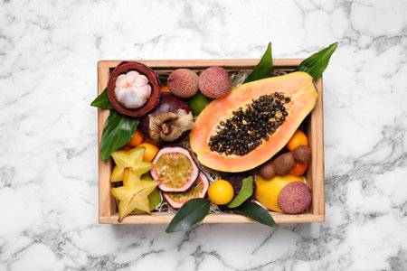 Different tropical fruits in wooden box on white marble table, top viewの写真素材