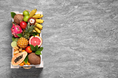 Different tropical fruits in wooden box on gray background, top view. Space for textの写真素材