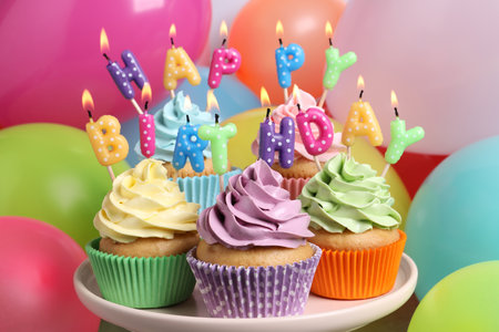 Birthday cupcakes with burning candles on stand near color balloons, closeupの写真素材