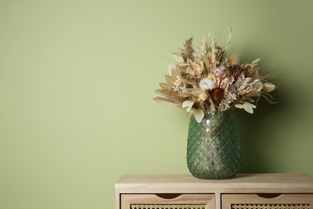 Beautiful flower dried bouquet in glass vase on wooden table near olive wall. Space for textの写真素材