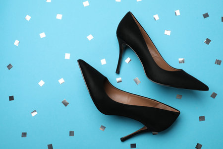 Pair of elegant black high heel shoes and confetti on light blue background, flat lay. Space for textの写真素材