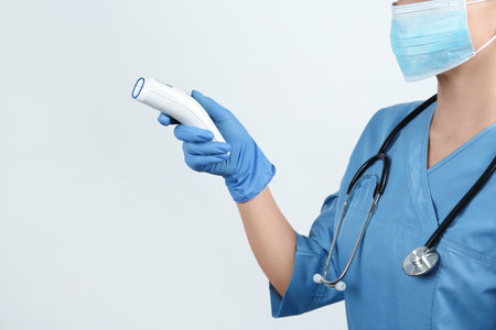 Doctor with infrared thermometer on light background, closeup.の写真素材