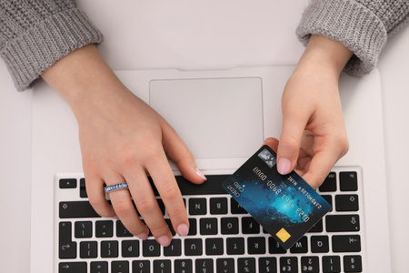Woman with credit card using laptop for online shopping at white table, top view