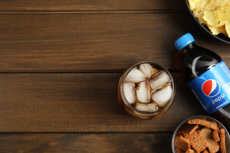 MYKOLAIV, UKRAINE - FEBRUARY 15, 2021: Glass and bottle of Pepsi with snacks on wooden table, flat lay. Space for textのeditorial素材