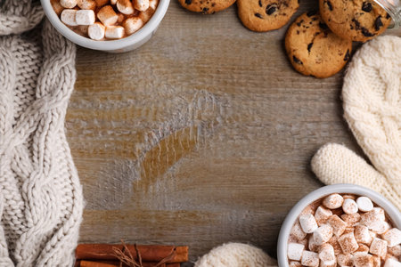 Frame made with cocoa drink, cookies and warm clothes on wooden table, flat lay. Space for textの写真素材