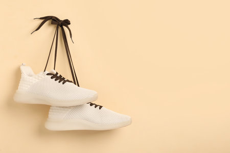 Stylish sneakers with brown shoe laces hanging on beige wall. Space for textの写真素材
