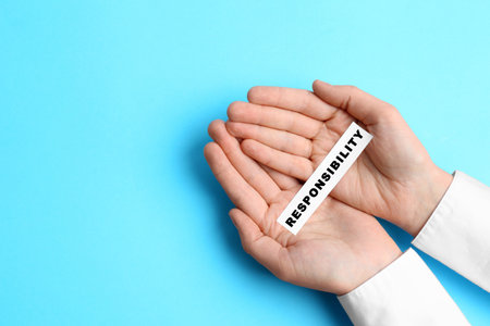 Woman holding paper with word Responsibility on light blue background, top view. Space for textの写真素材