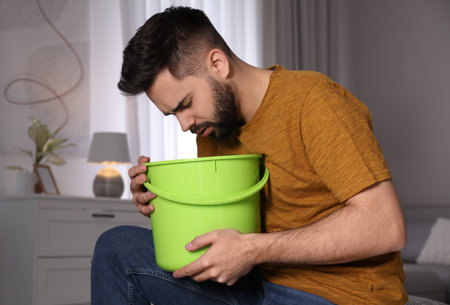 Young man with bucket suffering from nausea at home. food poisoningの写真素材
