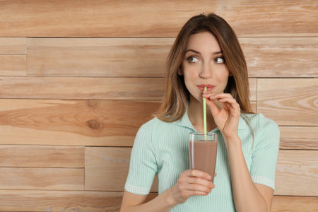 Young woman drinking chocolate milk on wooden background. Space for textの写真素材