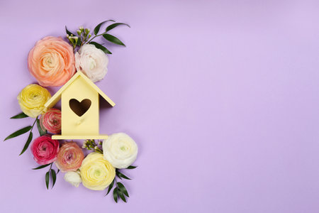 Stylish bird house and fresh flowers on violet background, flat lay. Space for textの写真素材