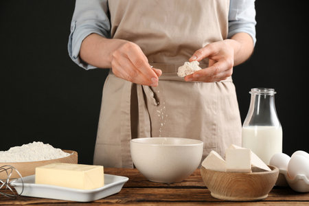Woman with compressed yeast and dough ingredients on wooden table, closeup