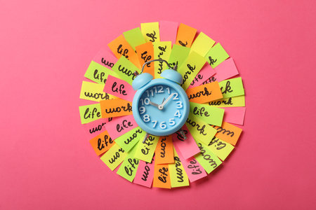 Alarm clock and many colorful paper pieces on pink background, top view. Life work balance conceptの写真素材