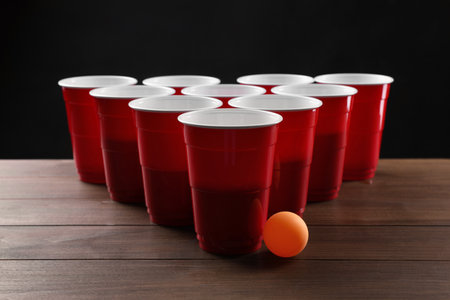 Plastic cups and ball for beer pong on wooden table against black backgroundの写真素材