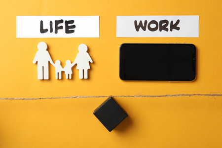 Family figures, smartphone and black cube on yellow wooden table, flat lay. Life work balance conceptの写真素材