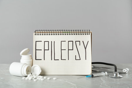 Notebook with word Epilepsy, stethoscope, pills and syringe on gray marble tableの写真素材
