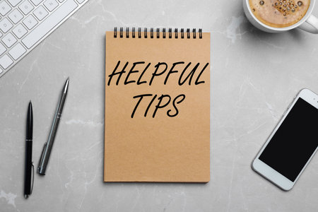 Notebook with text Helpful Tips, smartphone and cup of coffee on gray background, flat layの写真素材